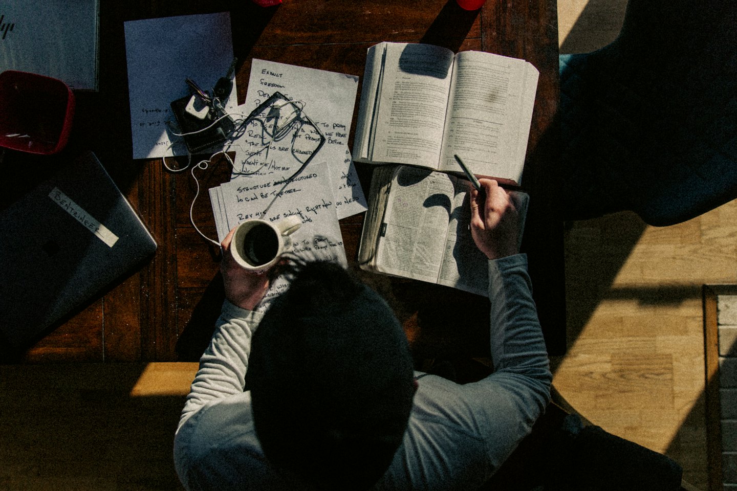 Person holding a mug and pen over notes on a desk.
